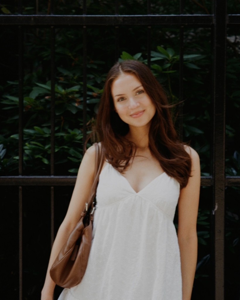 Dina in a white dress in front of a garden fence